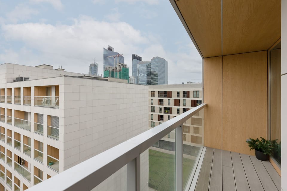 A balcony with a wooden finish and a view of the modern residential complex and surrounding greenery.

