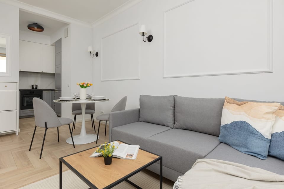 A wide-angle shot of the living area, featuring a gray sofa, stylish coffee table, and open layout connecting to the dining space.
