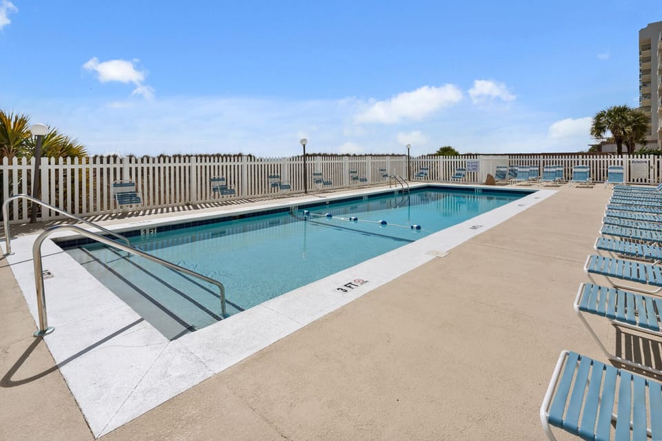 Poolside loungers behind a white picket fence at Crescent Sands of Windy Hill C2, a 3-bedroom rental in North Myrtle Beach