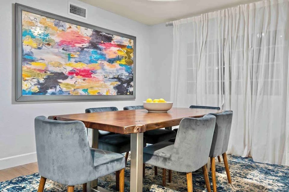 Dine in style with this sleek setup featuring a bold, vibrant artwork centerpiece and a rustic hardwood table and plush seats for a cozy atmosphere perfect for any meal! 