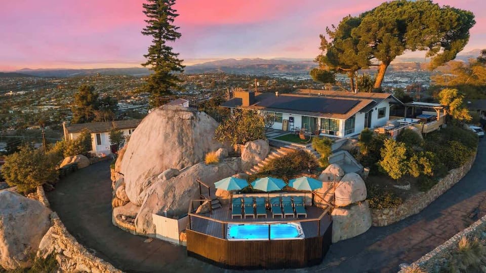 Overlooking the city at approx 600 feet above sea level, this 1.39-acre property features a wooden deck with lounge chairs, a swim spa, and natural boulders, all set amidst a well-maintained landscape. Perfect to unwind and enjoy the stunning views.