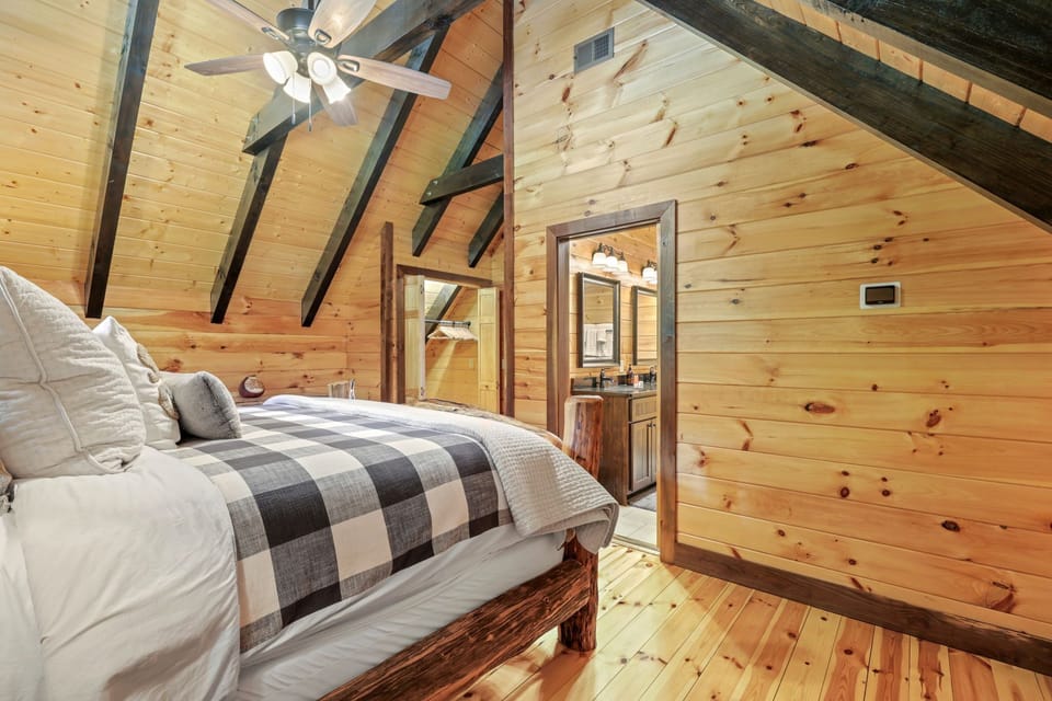 Upper level bedroom featuring a log bed, vaulted ceiling, wood flooring, and direct access to the adjoining bathroom. Enjoy cozy cabin accommodations in the Smoky Mountains near Bryson City.