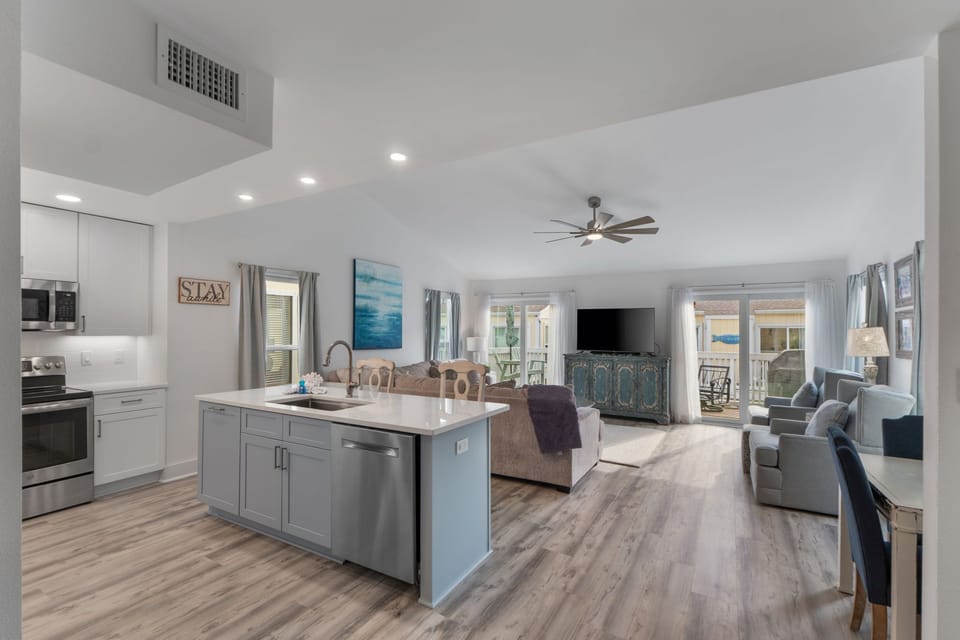 Relax in your open-concept living space with modern kitchen, comfy seating, and peaceful ocean artwork creating a coastal vibe.