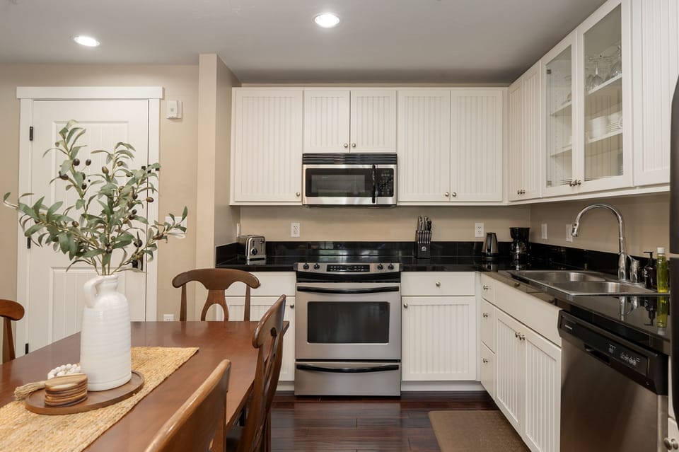 A modern kitchen with white cabinets, black countertops, stainless steel appliances, a wooden dining table set with chairs
