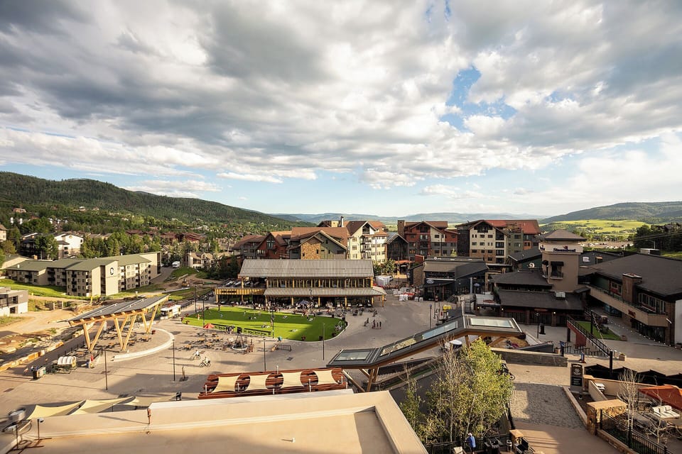 Panoramic mountain village setting with rolling hills and forested landscape surrounding the resort area.