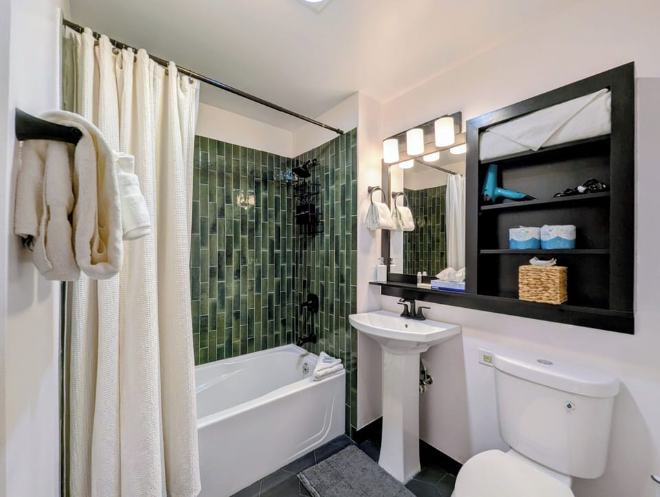 Your private bathroom features elegant green tile, a soaking tub, and built-in shelves stocked with plush robes and fresh towels for a relaxing retreat.