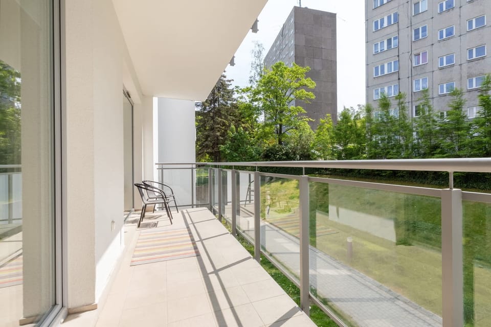 A spacious balcony with glass railings offering a serene view of the surrounding garden and outdoor spaces.