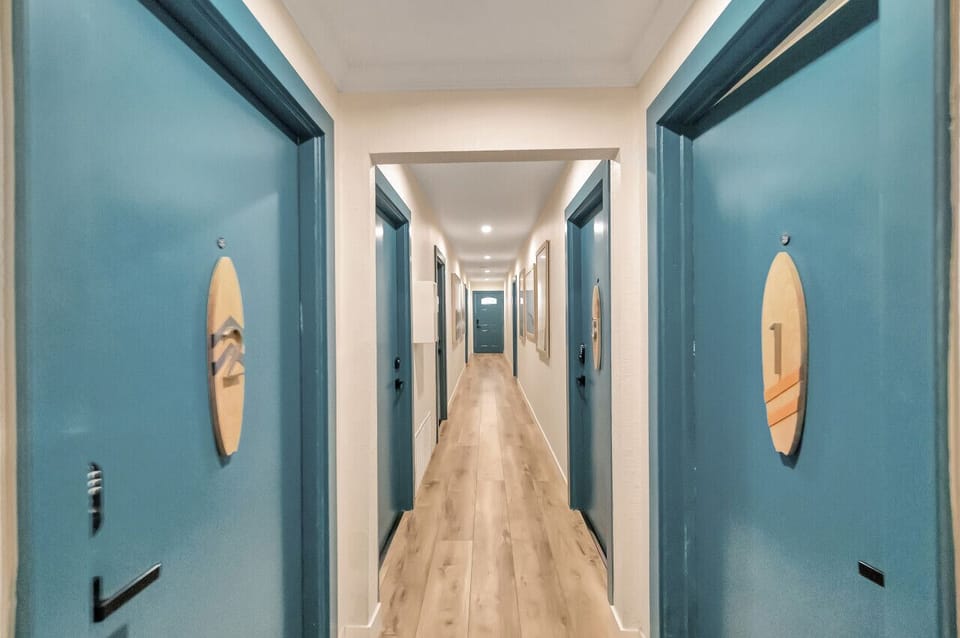 Clean hallway w/ teal doors & wood floors leading to guest suites