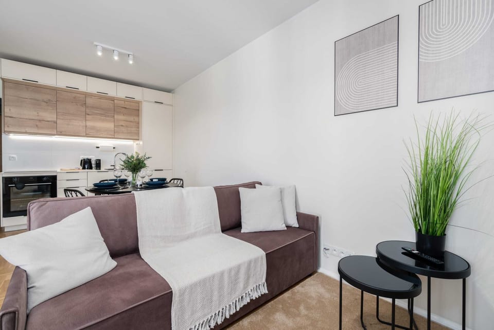 A modern living room with a light-colored sofa, coffee table, and windows allowing natural light.