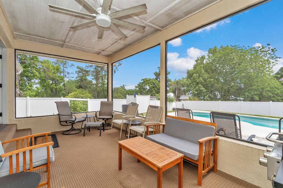 Screened Florida room with seating, ceiling fan, BBQ, overlooking heated pool