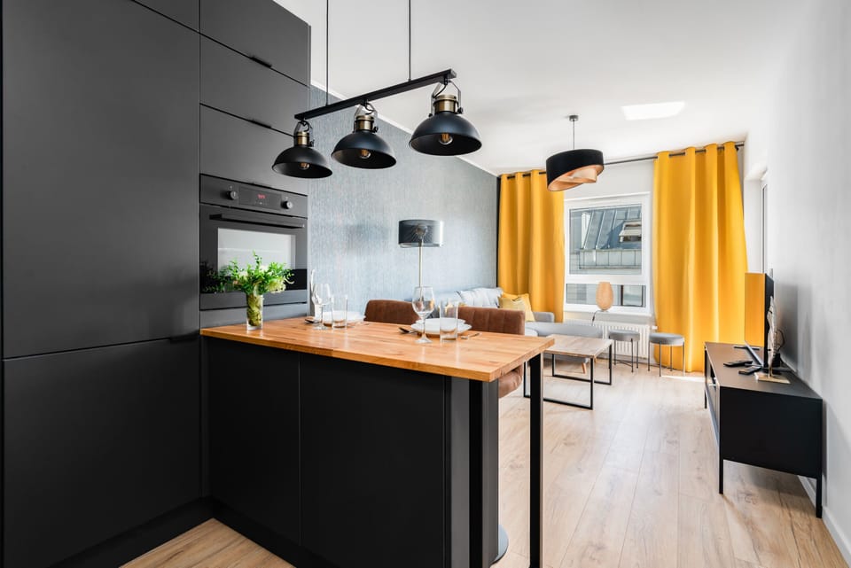 A sleek black-and-wood kitchen paired with a cozy dining area, illuminated by stylish pendant lights.