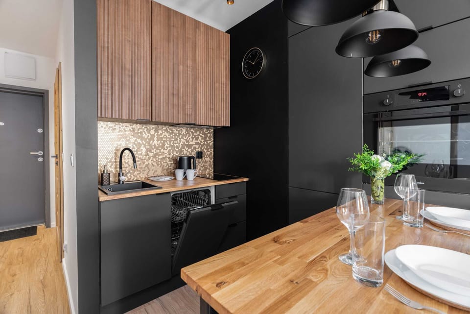 A sleek black-and-wood kitchen paired with a cozy dining area, illuminated by stylish pendant lights.