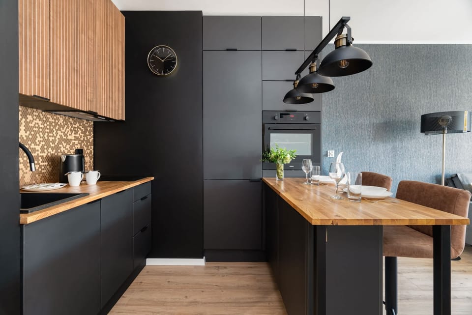 A sleek black-and-wood kitchen paired with a cozy dining area, illuminated by stylish pendant lights.