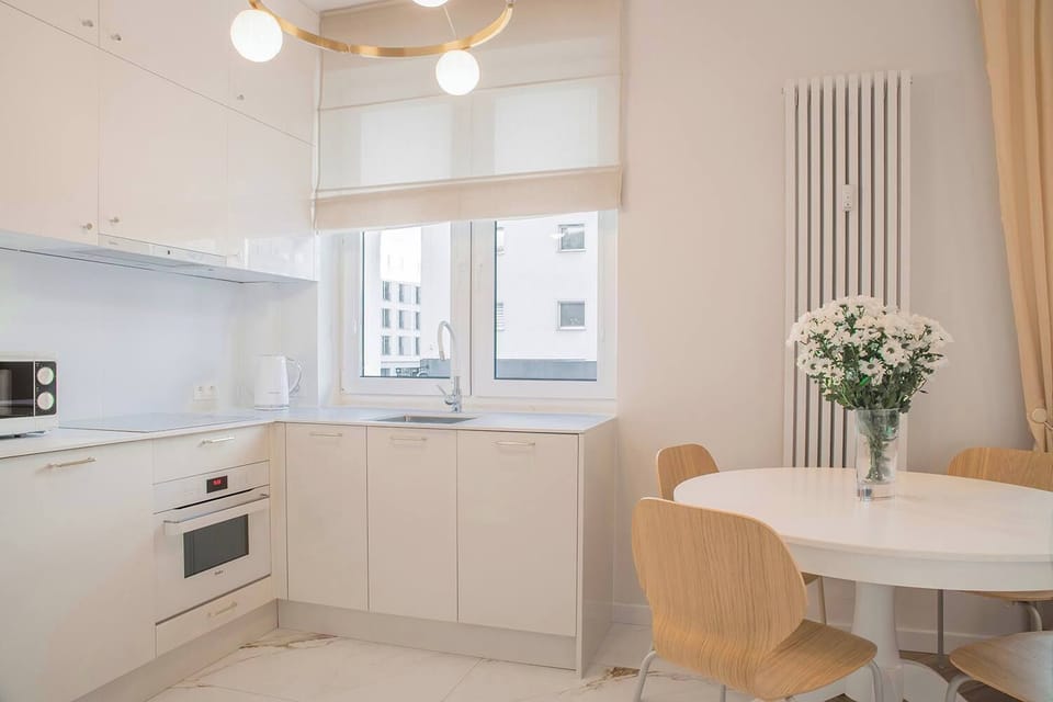Modern white kitchen with dining area – Fully equipped kitchen with built-in appliances and natural daylight.