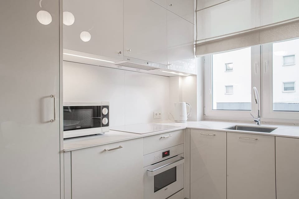 Compact modern kitchen with built-in appliances – Sleek white kitchen with oven, microwave, and under-cabinet lighting.