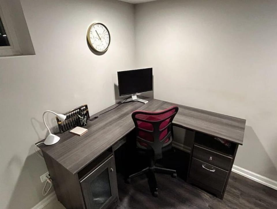 Basement workspace with monitor, desk lamp, and office supplies.