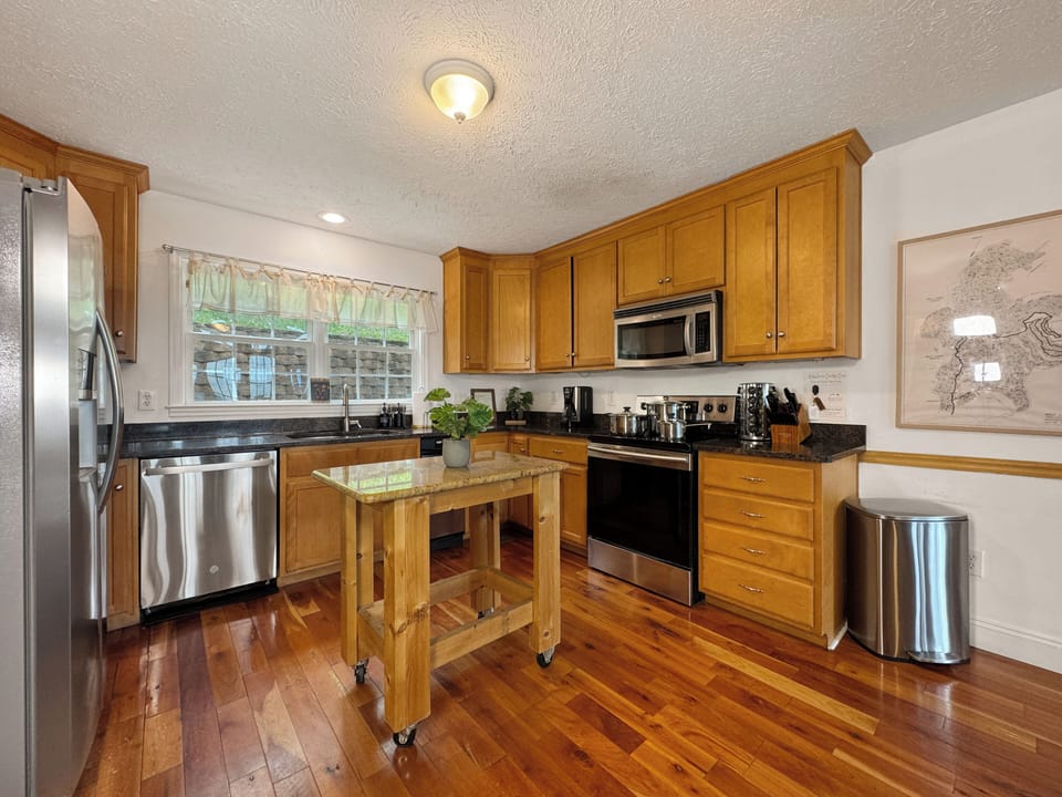 This charming kitchen features a small butcher block island perfect for meal prep, flowing into a spacious dining area with a large table—ideal for family meals, game nights, or gathering with friends after a day of mountain adventures.
