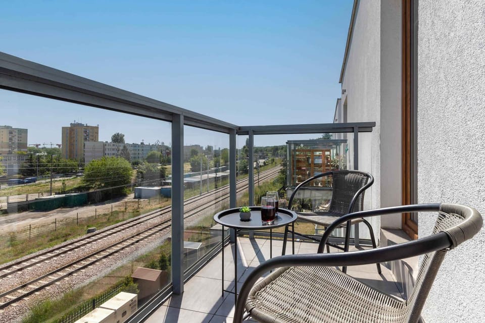 A private balcony equipped with a table and chairs, overlooking a modern urban neighborhood.