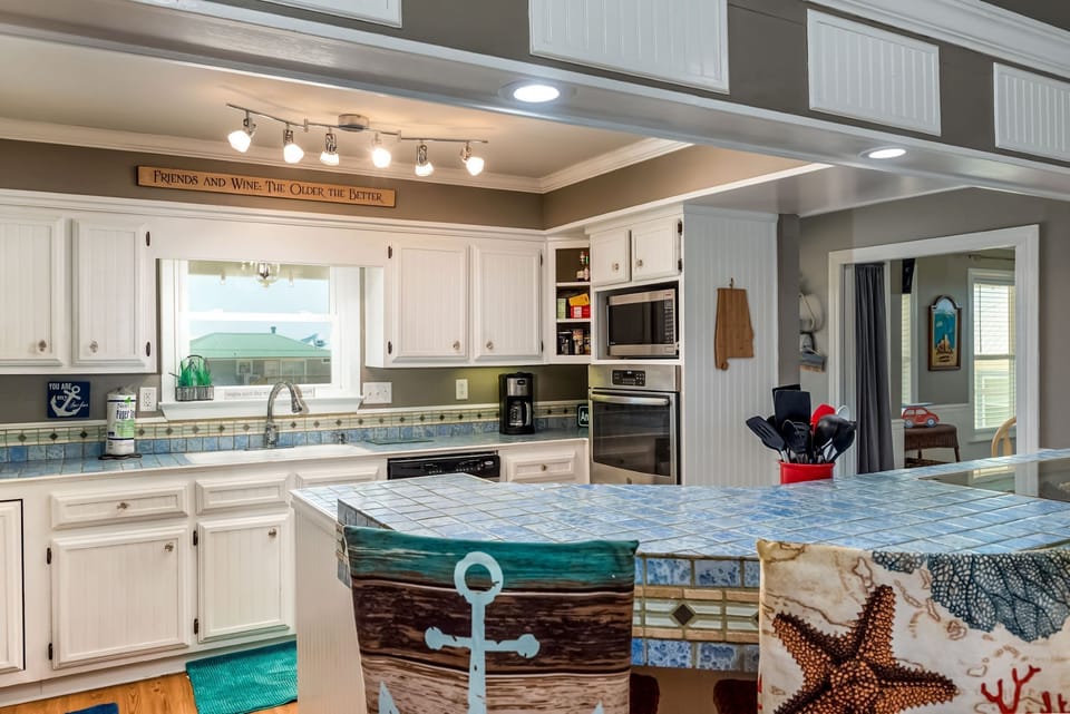 Your fully equipped kitchen features coastal charm with white cabinets, tile counters, and modern appliances—perfect for preparing meals with ocean views.