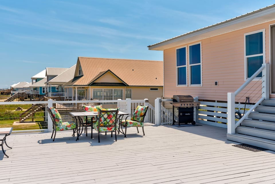 Spacious deck with colorful patio furniture and gas grill, perfect for outdoor dining with coastal charm.