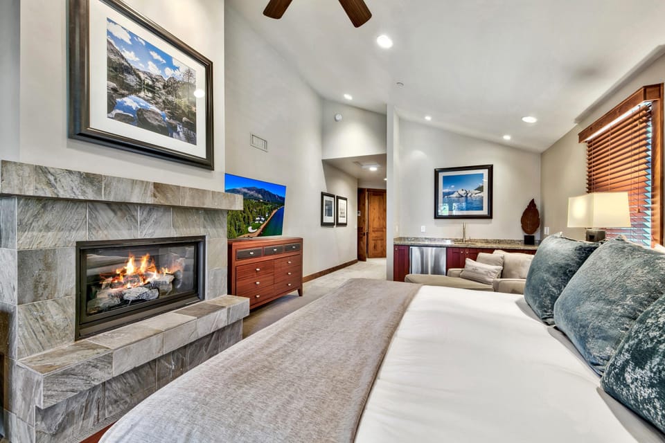 Bedroom with stone-tiled gas fireplace, wooden dresser, granite wet bar, and soft blue velvet pillows on bed.