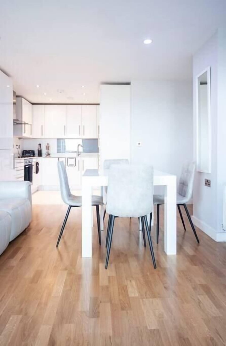A modern living room on the 12th floor features a 60-inch TV, a dining table with four chairs, and access to a balcony with stunning city views. Two electric reclined sofas provide comfort and a sound system offer entertainment.
