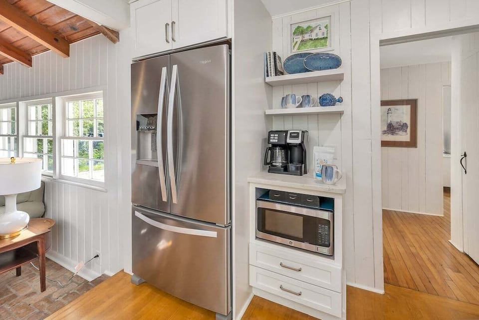 White kitchen with stainless fridge, microwave, and open shelving