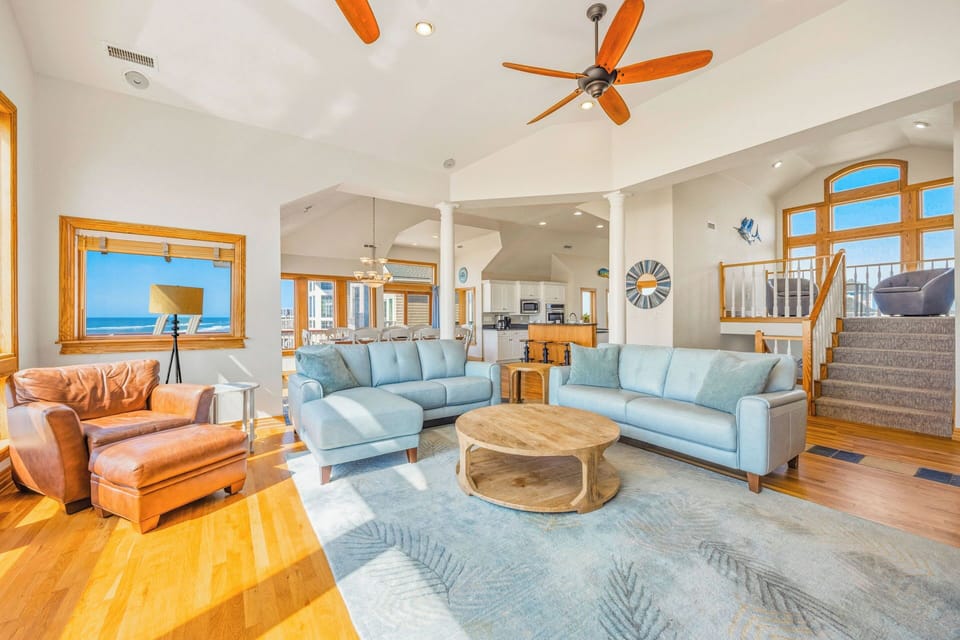 Relax in your bright, open living space with soaring vaulted ceilings, coastal breezes from ceiling fans, and stunning ocean views framed by warm wood accents inviting you to unwind.