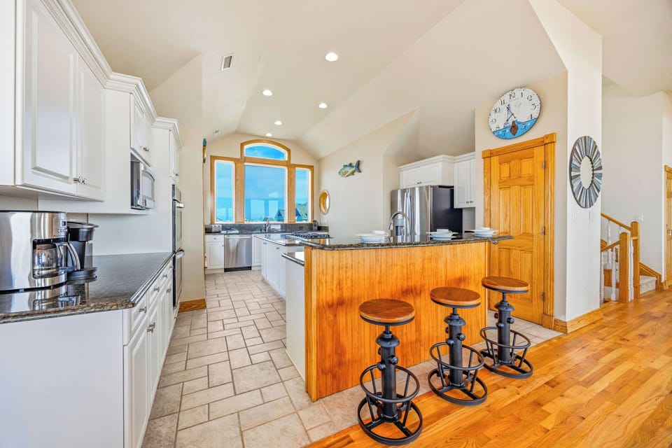 Your spacious kitchen blends coastal charm with modern convenience—cook meals at granite counters, gather at the warm wood island, and enjoy stunning ocean views through the arched windows.