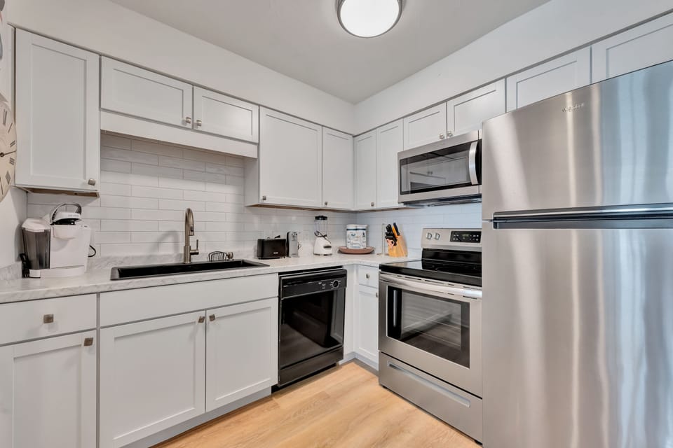 Your fully equipped modern kitchen awaits with stainless steel appliances, sleek white cabinetry, and warm hardwood floors perfect for preparing meals.