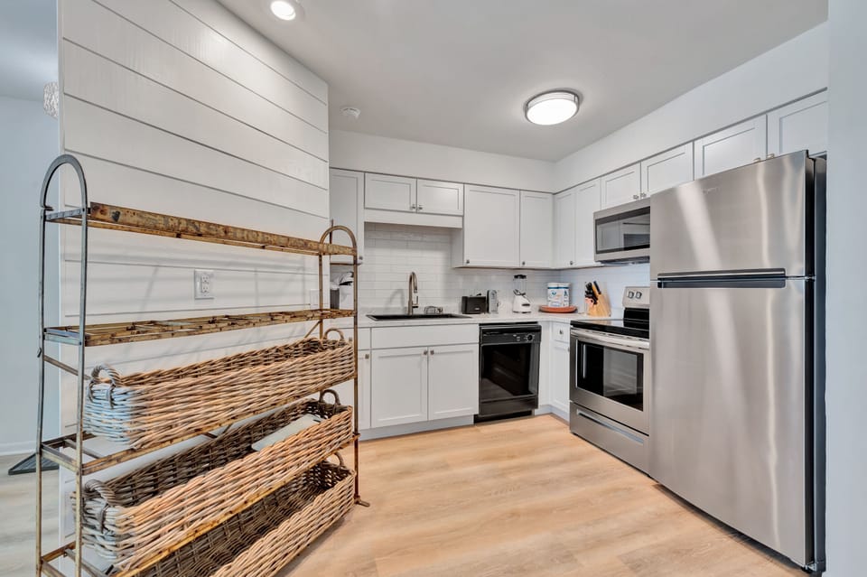 Your fully equipped kitchen invites culinary adventures with stainless steel appliances, crisp white cabinets, and charming wicker storage adding warmth to your stay.