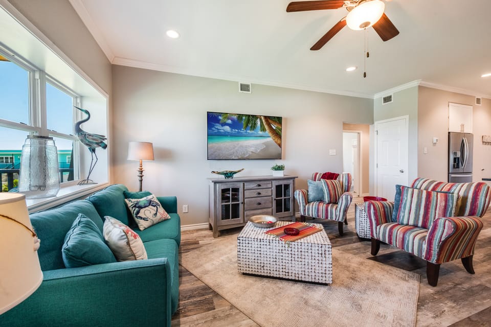 Unwind in your bright living room featuring a cozy teal sofa, colorful striped chairs, and tropical artwork—perfect for relaxing after beachside adventures.
