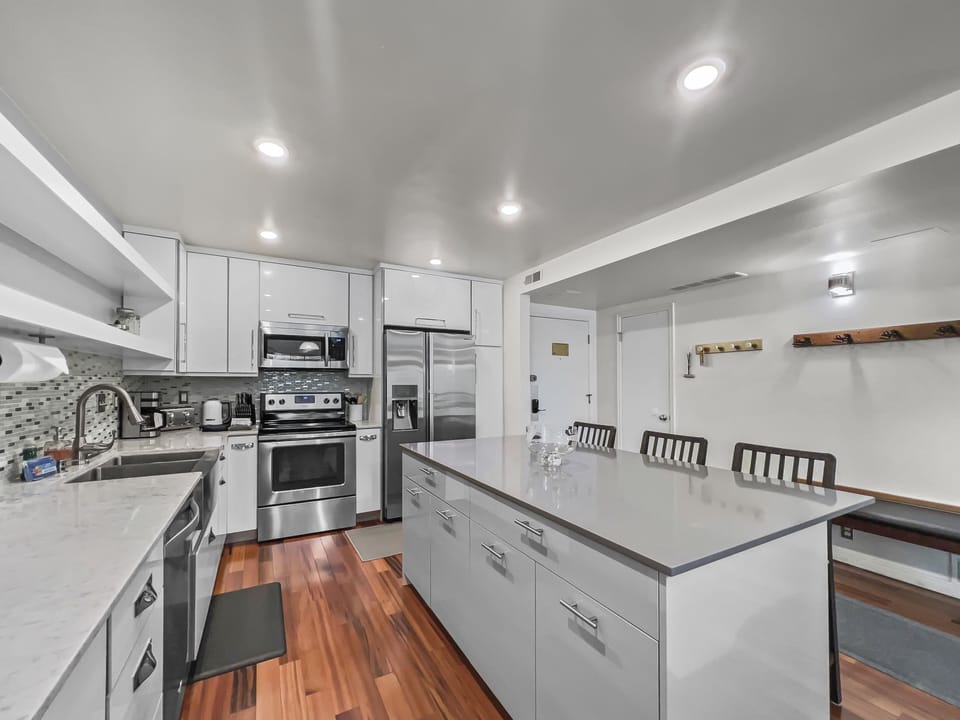 Prepare meals in our fully equipped kitchen, featuring a large island with bar seating, modern stainless steel appliances, and stylish two-tone design. All the essentials for a great stay.