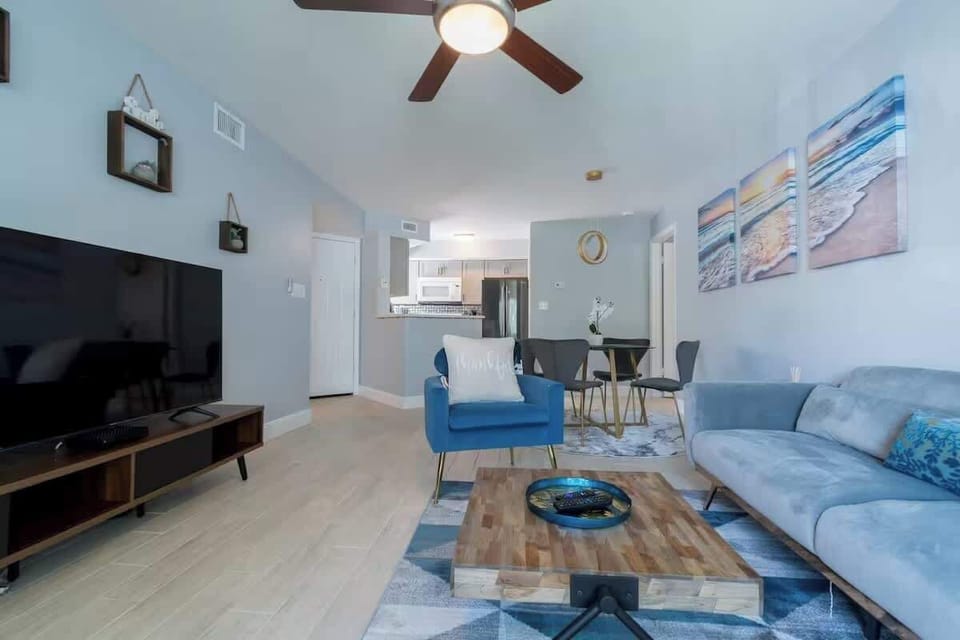 Open living area with a sectional, accent chair, and large TV, flowing into the dining space and kitchen beyond.
