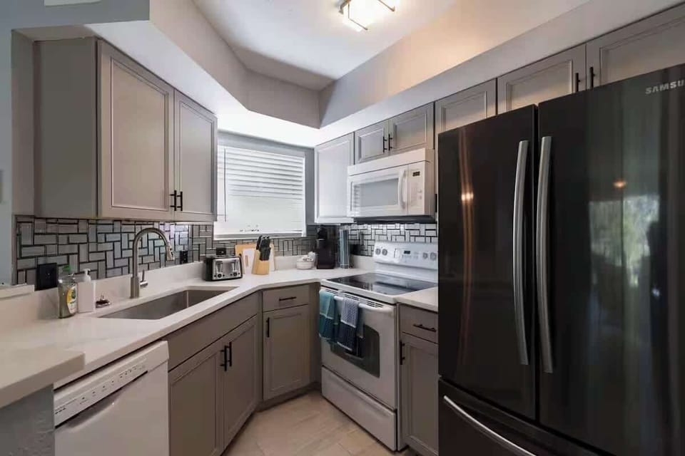 Compact kitchen with full-size appliances, a double sink, and tile backsplash.