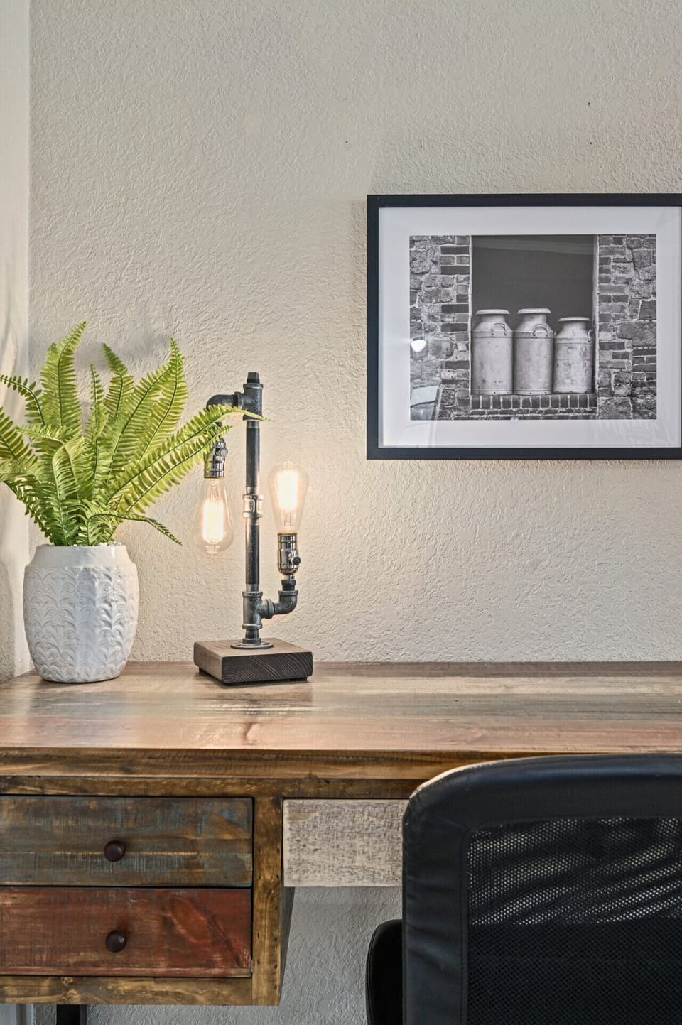 Dedicated workspace at Saloma Place featuring rustic desk, comfy chair, and warm industrial lamp—perfect for remote work or catching up on email.