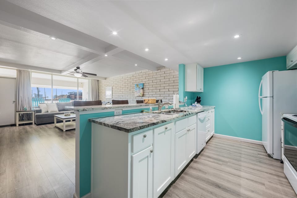 Prepare meals in your vibrant kitchen with granite countertops, white cabinetry, and turquoise accents that flow into the bright living area.