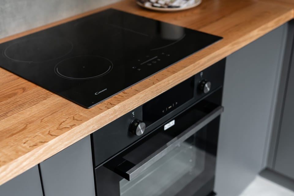 A modern stovetop and oven setup with a wooden countertop, showcasing a stylish and functional kitchen design.
