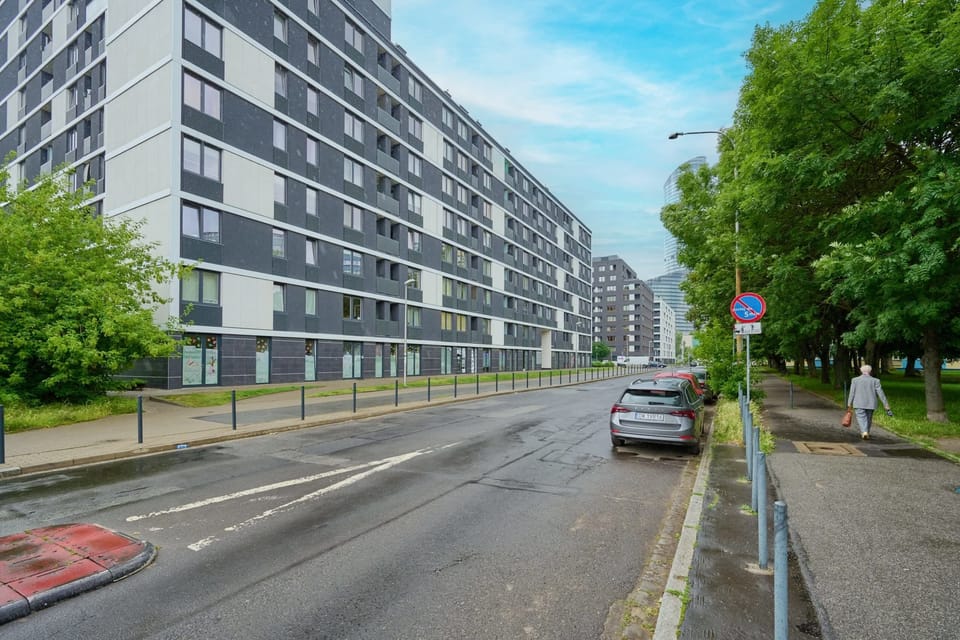 View of the building from the street, with a tree-lined road and parking spaces.
