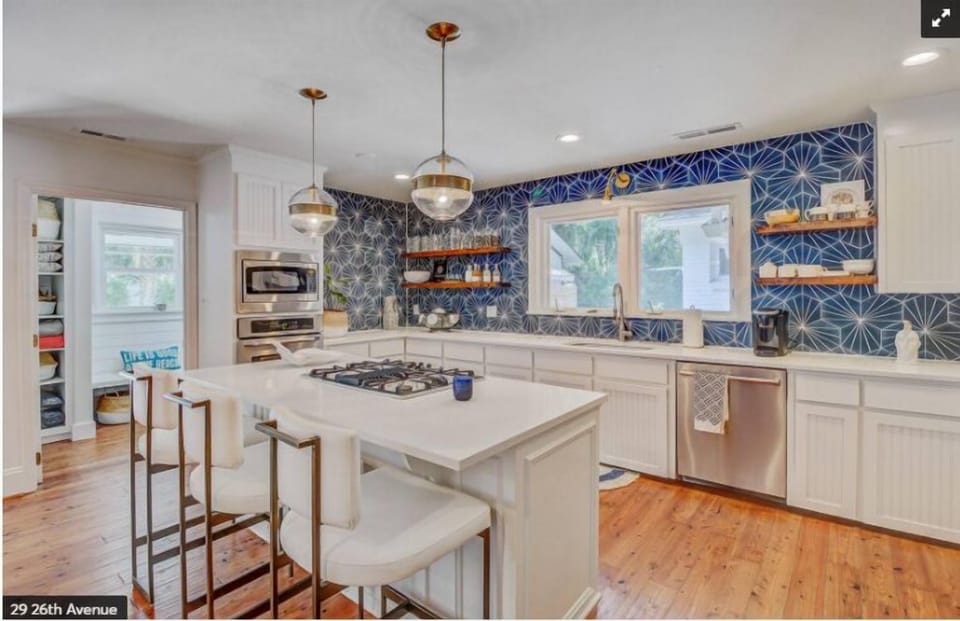 Modern kitchen with a white island, bar stools, and blue geometric tile backsplash.