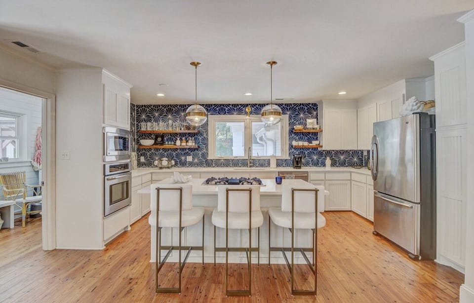 Modern kitchen with white cabinets, blue patterned backsplash, island with four white bar stools, and stainless steel appliances.