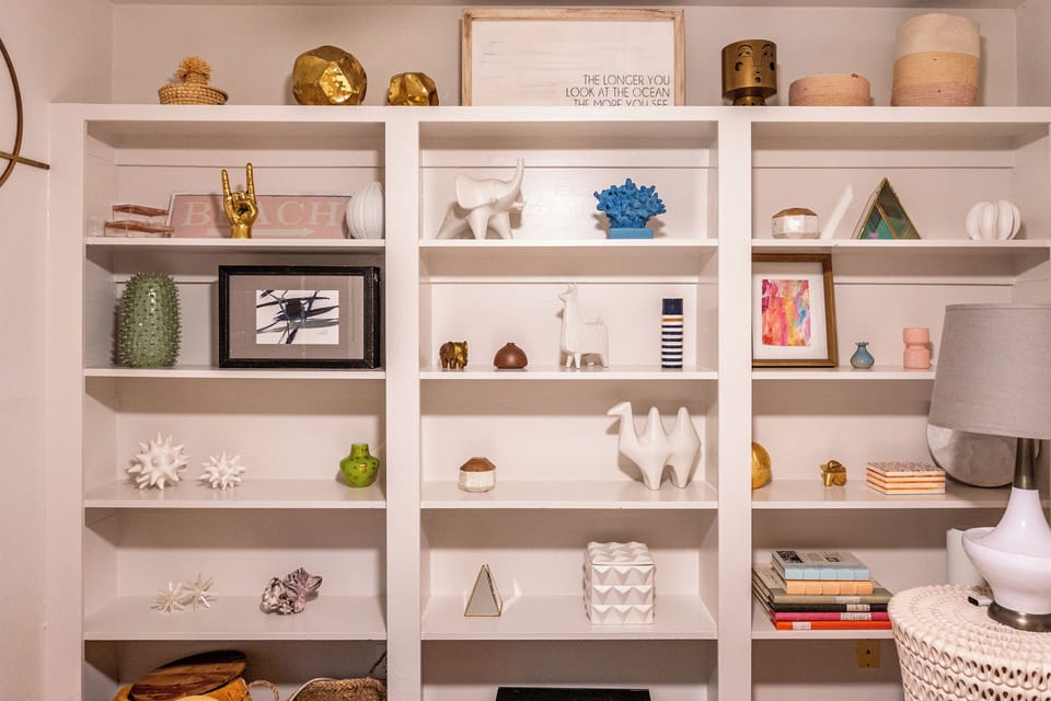 A white shelving unit with decorative items including sculptures, books, and small artworks.