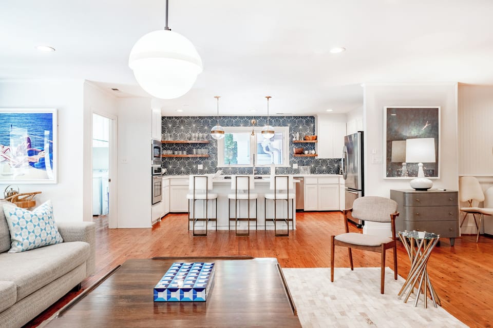 Three modern counter stools trimmed in brass. with a view into the kitchen. Large window above the sink.