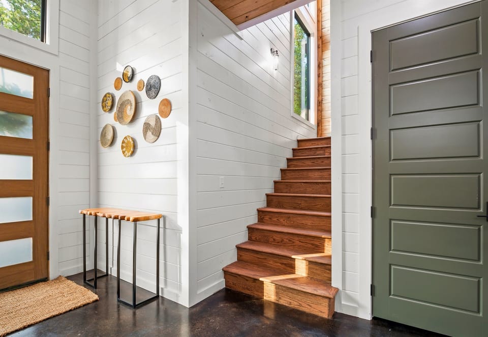 The entryway is highlighted by a staircase with warm wooden steps and a decorative wall of metallic art pieces, creating a dynamic and welcoming space.