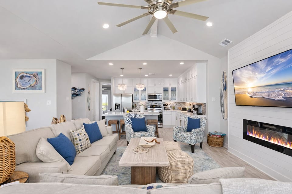 Spacious living room with modern furnishings, ceiling fan, fireplace, and seamless flow into kitchen and dining areas.