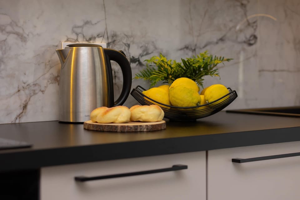 The kitchen is modern and fully equipped, with white countertops, sleek cabinets, and stainless-steel appliances. A decorative arrangement of lemons and a kettle on the counter adds a welcoming touch.
