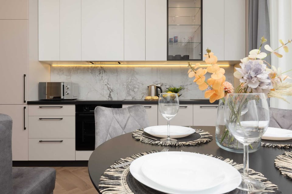 The dining area is stylishly set up with a round table, chic chairs, and tableware, perfect for a cozy meal. The open-plan layout connects seamlessly with the living room.
