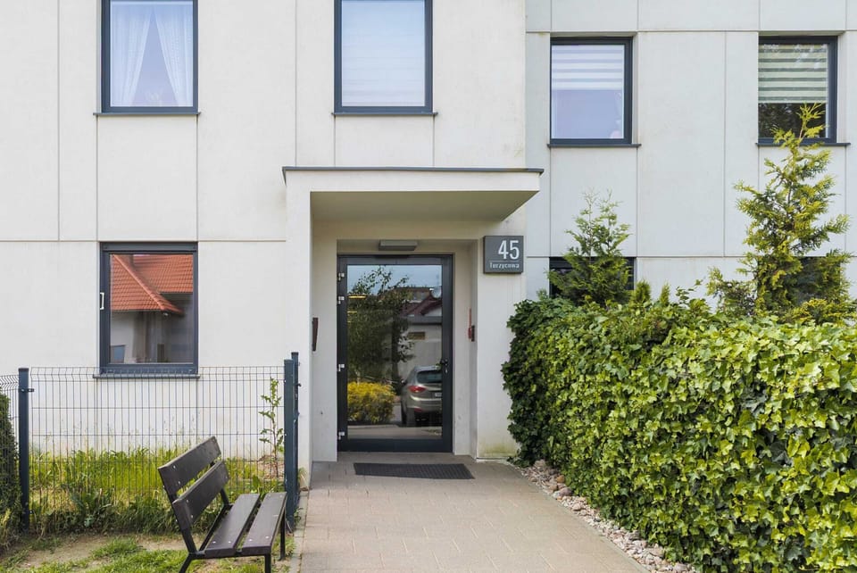A modern building entrance with a neat pathway surrounded by greenery and a hedge for privacy.