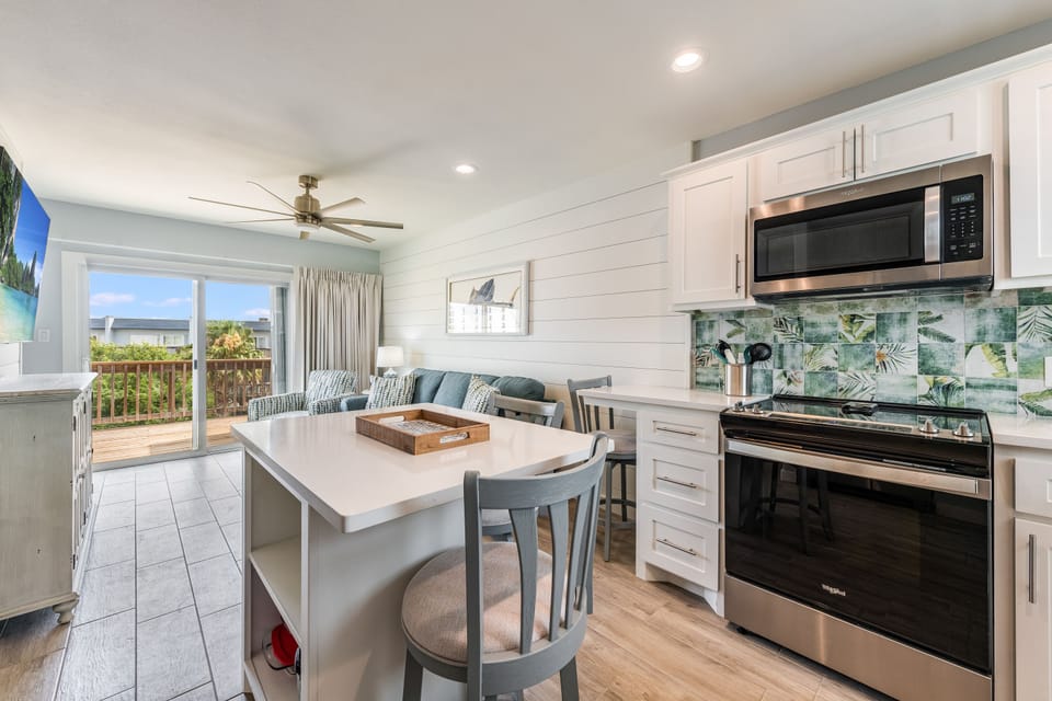 Your modern kitchen invites culinary adventures with tropical-inspired backsplash, sleek appliances, and island seating perfect for morning coffee.