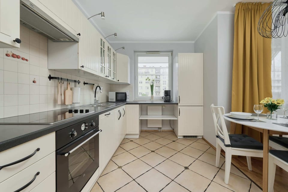 A full view of the kitchen, featuring modern appliances, plenty of counter space, and a dining area with yellow curtains.
